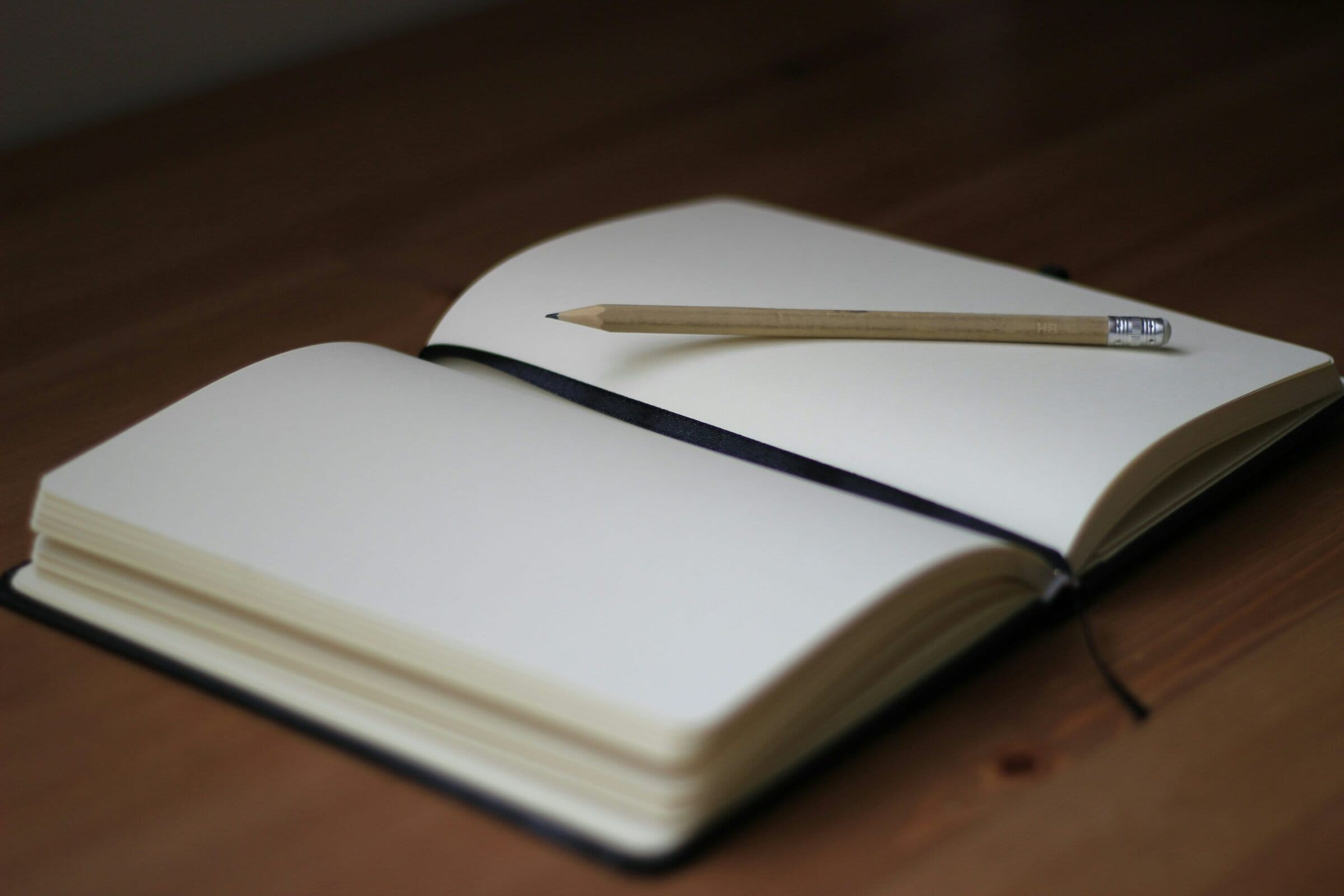 An open unlined notebook with a pencil lying on it